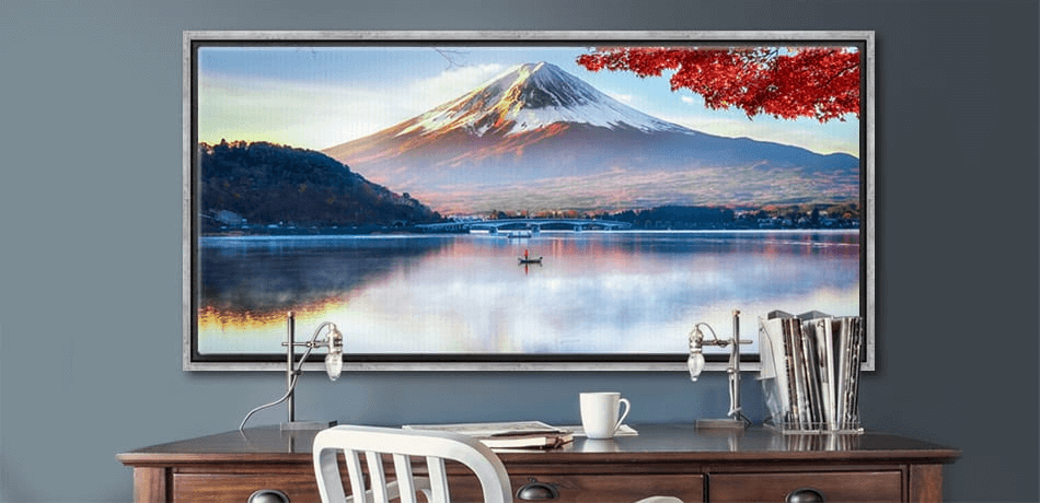 Large framed landscape photograph of Mount Fuji reflected on a lake, displayed above a wooden desk with books, lamps, and coffee mug