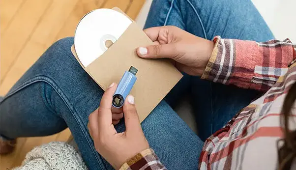Person holding a USB drive and CD in paper sleeve preparing audio media for digital transfer
