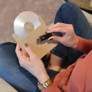 Person holding a disc and USB drive representing digitized photo and video archive storage formats