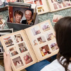Person looking through printed family photo albums and loose photographs on a table