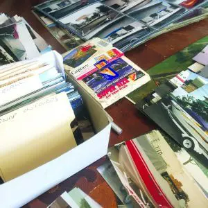 Collection of loose photographs and printed memorabilia spread across a table for archiving and scanning