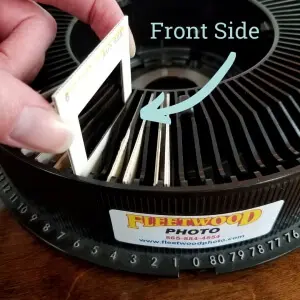 Hand placing a slide into a carousel slot with the front side facing right for proper slide scanning orientation