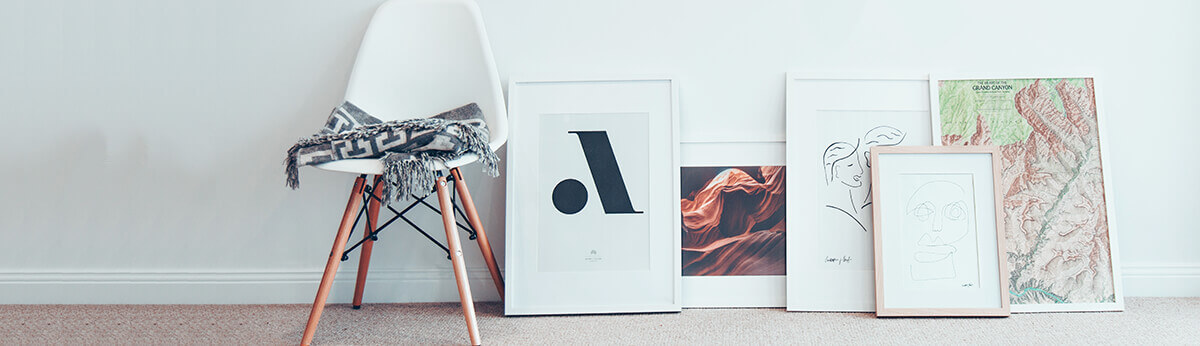 Assorted framed art prints leaning against a wall beside a chair in a modern home