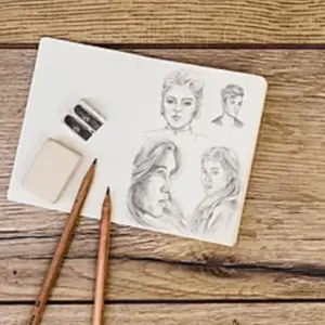 Hand-drawn pencil portrait sketches on paper with drawing tools on a wooden table