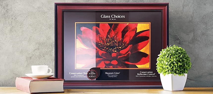 Custom framed artwork display showing glass protection options and reflection control samples in a wood frame on a tabletop