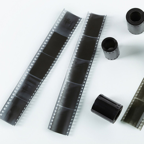 Strips of photographic film negatives laid out on a white surface with film canisters