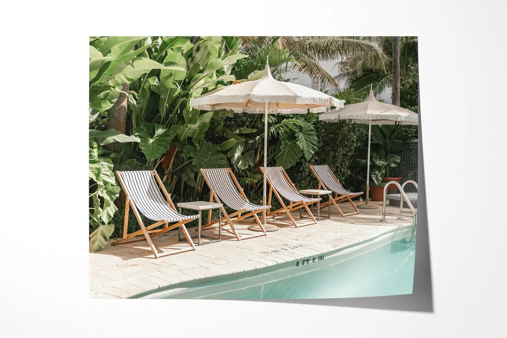A peel-and-stick photo print of a tropical poolside scene with lounge chairs and umbrellas, displayed on a white wall
