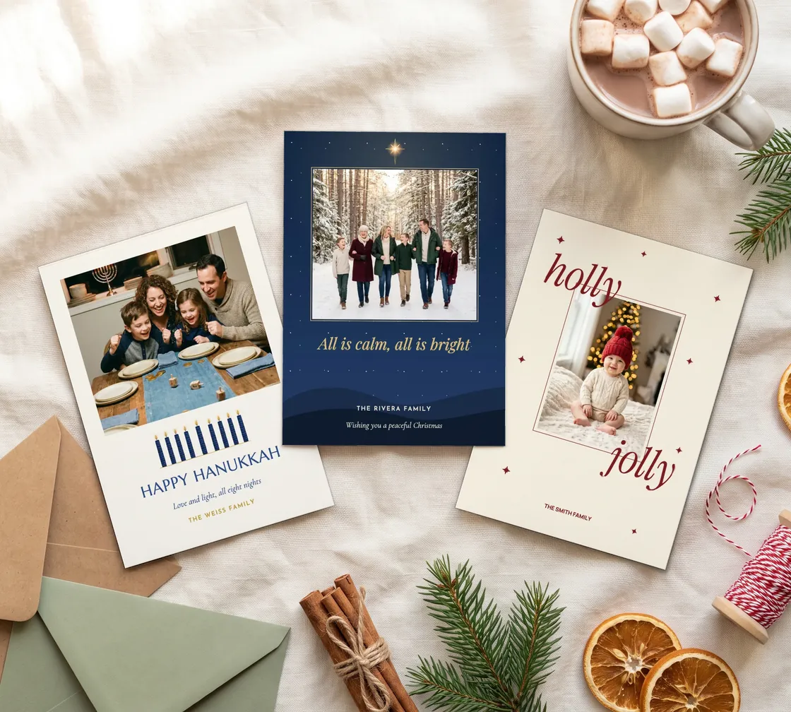 Three photo holiday cards laid flat with envelopes and winter trimmings