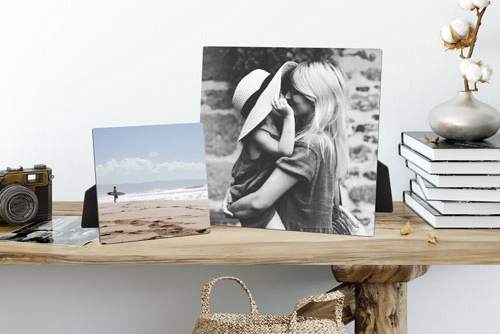 A wooden shelf displaying two easel-mounted photo prints, one black and white of a mother and child, and another of a beach scene