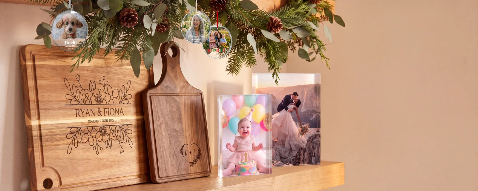 Personalized photo ornaments, engraved acacia and walnut cutting boards, and clear acrylic photo blocks on a wood shelf under a holiday garland