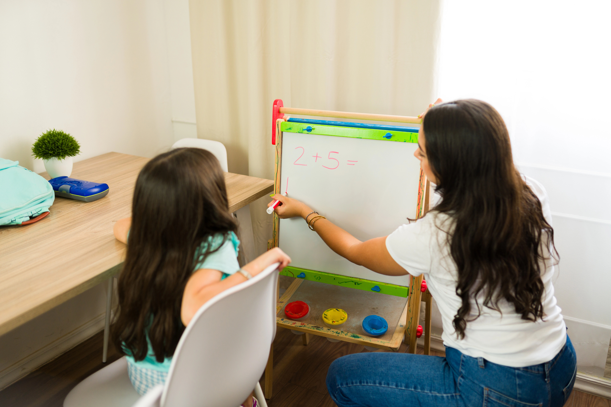 A homeschooled child learning math on a whiteboard from their parent.