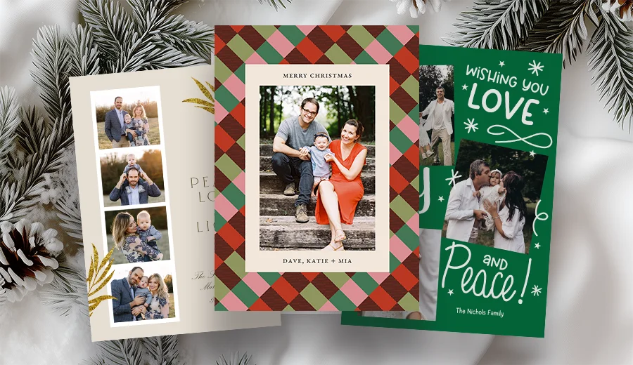 Custom printed holiday photo cards fanned out on a table with pine branches.