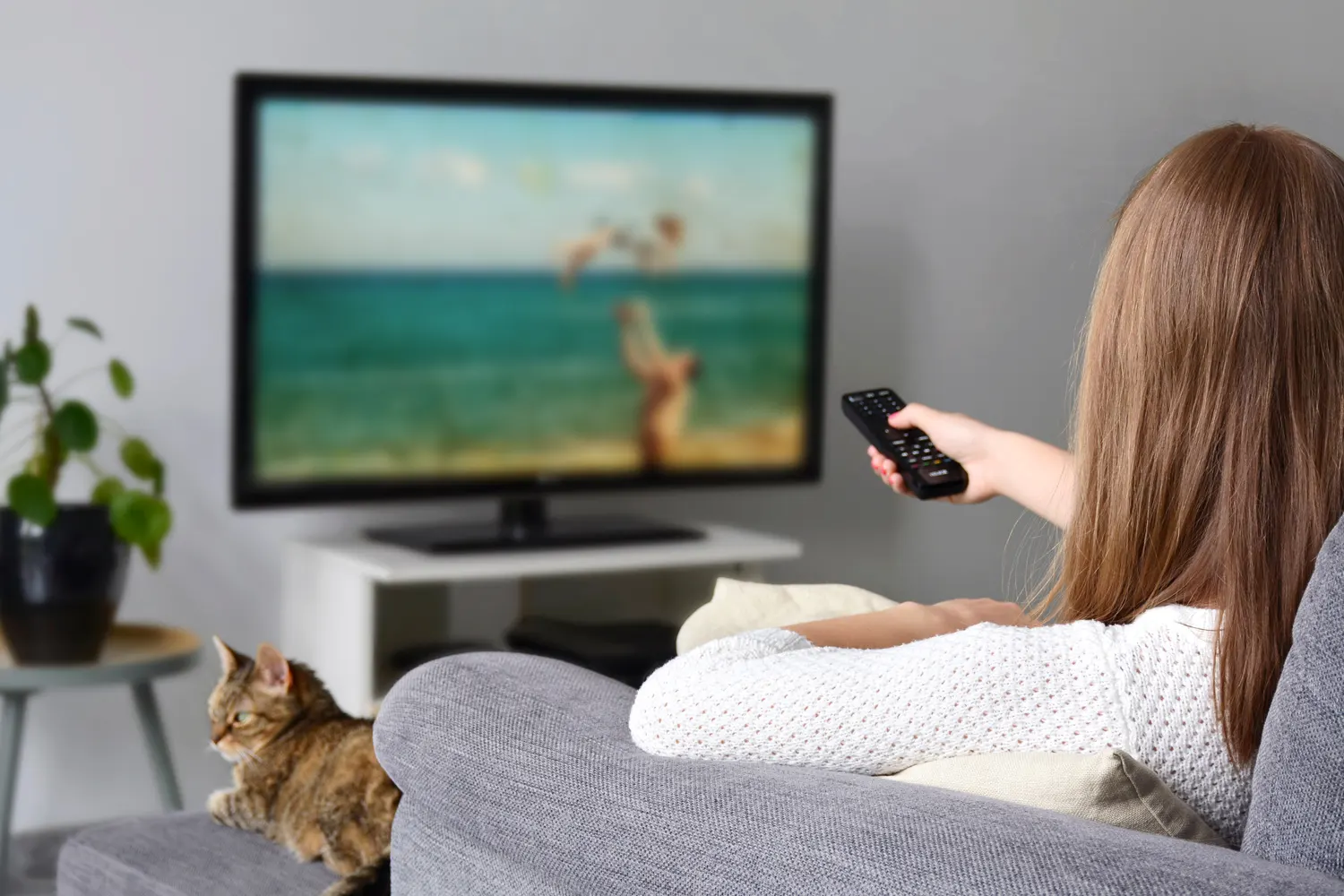 A woman watching a slideshow of beach memories on TV while relaxing with a cat, illustrating video slideshow services