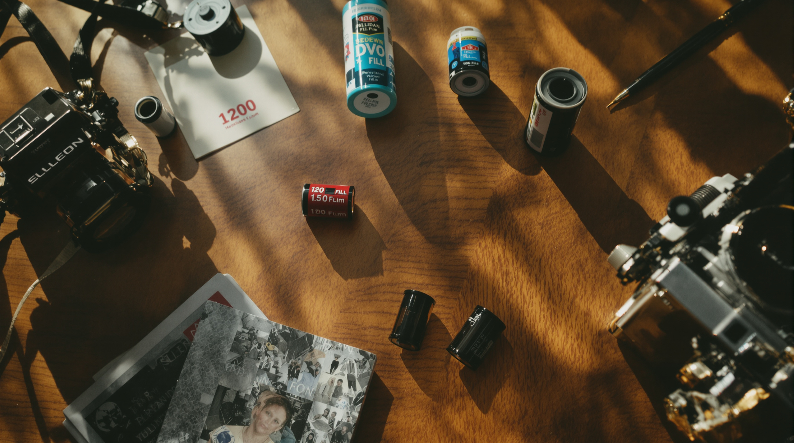 A flat lay photograph on a wooden table featuring rolls of 35mm film canisters, a 120 medium format roll, a disposable camera, and a vintage analog film camera, warm natural light, shallow depth of field, rich film-photography aesthetic