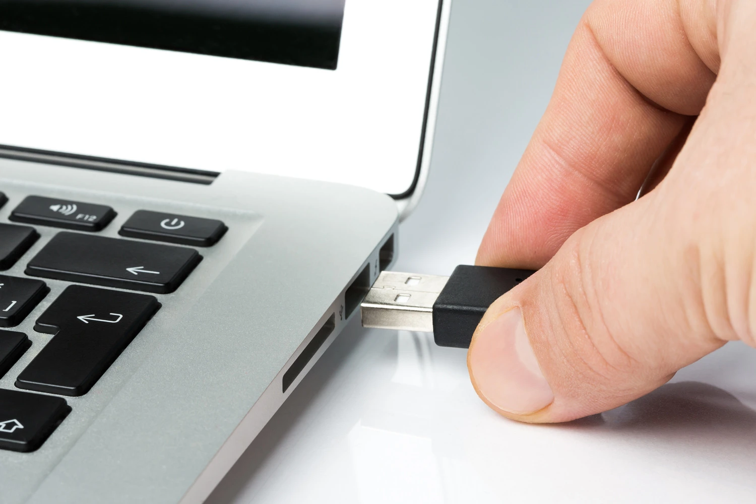 A hand inserting a USB drive into a laptop's USB port, illustrating data transfer or device connection