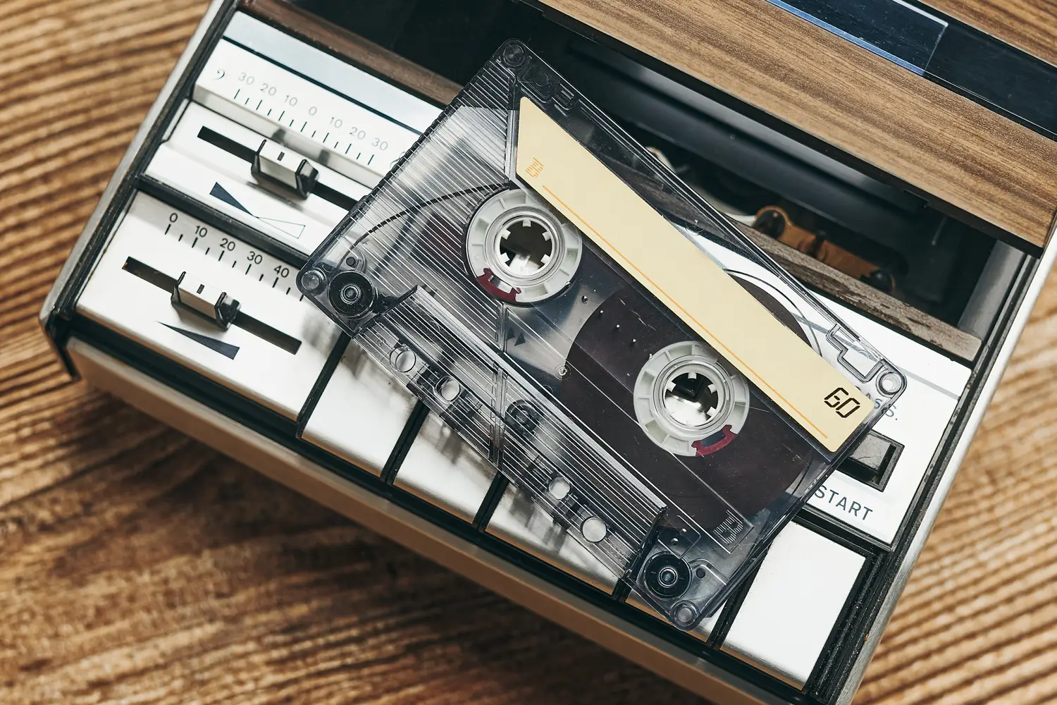 Close-up of a cassette tape placed on a vintage tape recorder, showing dials, sliders, and retro design
