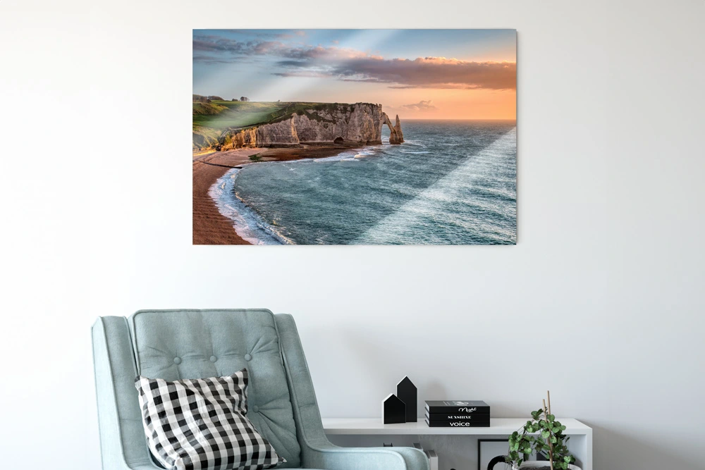 A modern living room with a large acrylic print of a coastal cliff at sunset hanging on a white wall above a blue armchair
