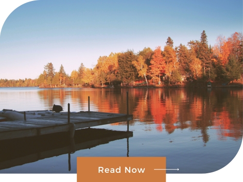 Dock overlooking calm lake with colorful fall foliage reflecting in the water