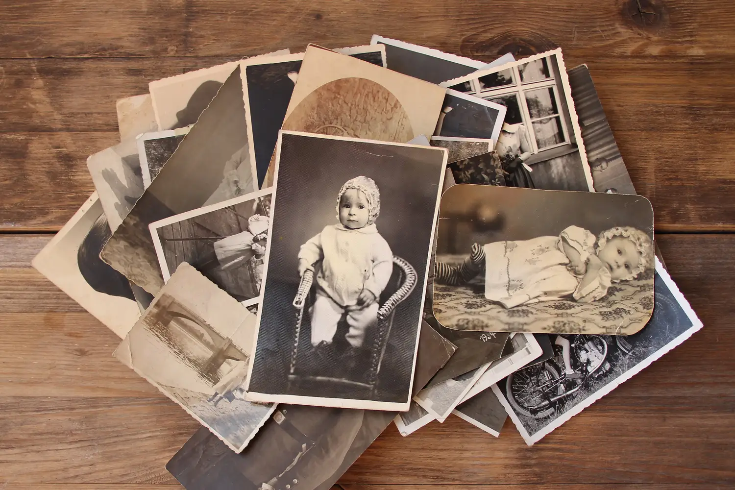 A pile of vintage black-and-white photographs, featuring portraits and scenic images, spread out on a wooden surface