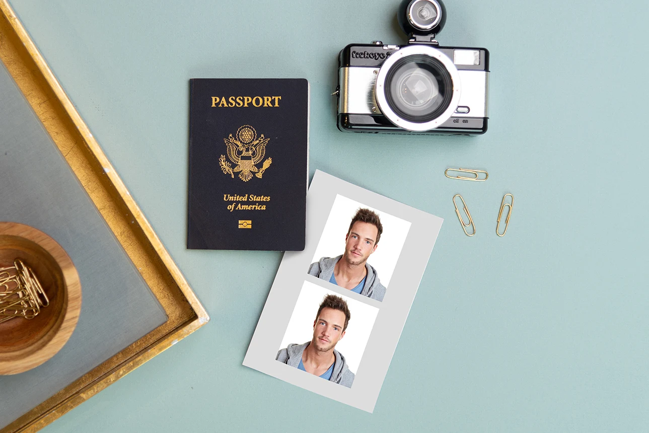 Flat lay featuring a U.S. passport, a vintage camera, gold paperclips, and printed passport photos of a man on a light teal background