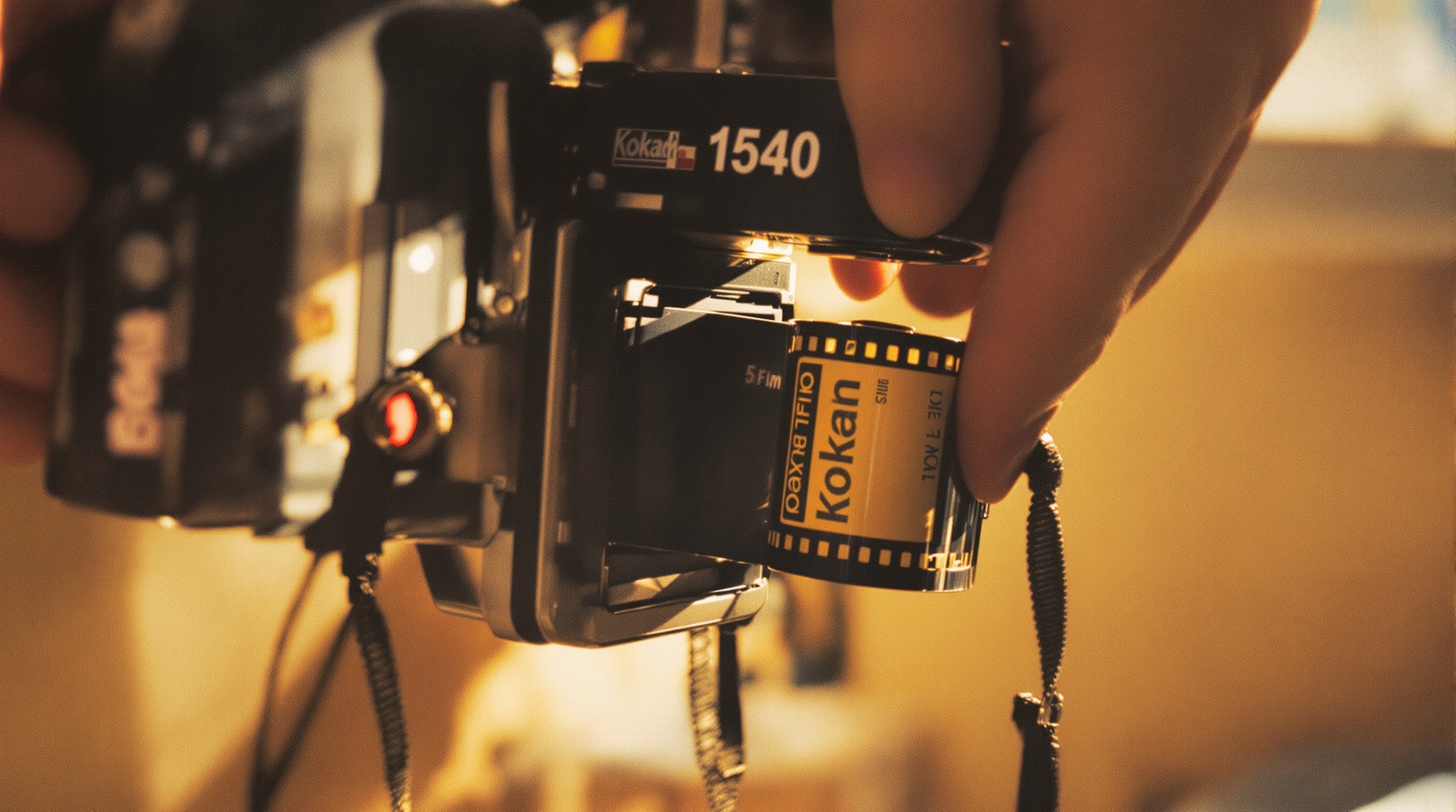Hands loading Kodak film roll into a vintage 35mm film camera near a sunlit window
