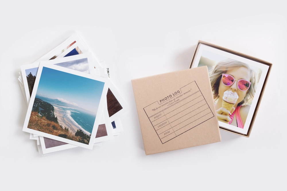 A set of square photo prints featuring travel and lifestyle images, neatly stacked and stored in a kraft photo log box with labeling space