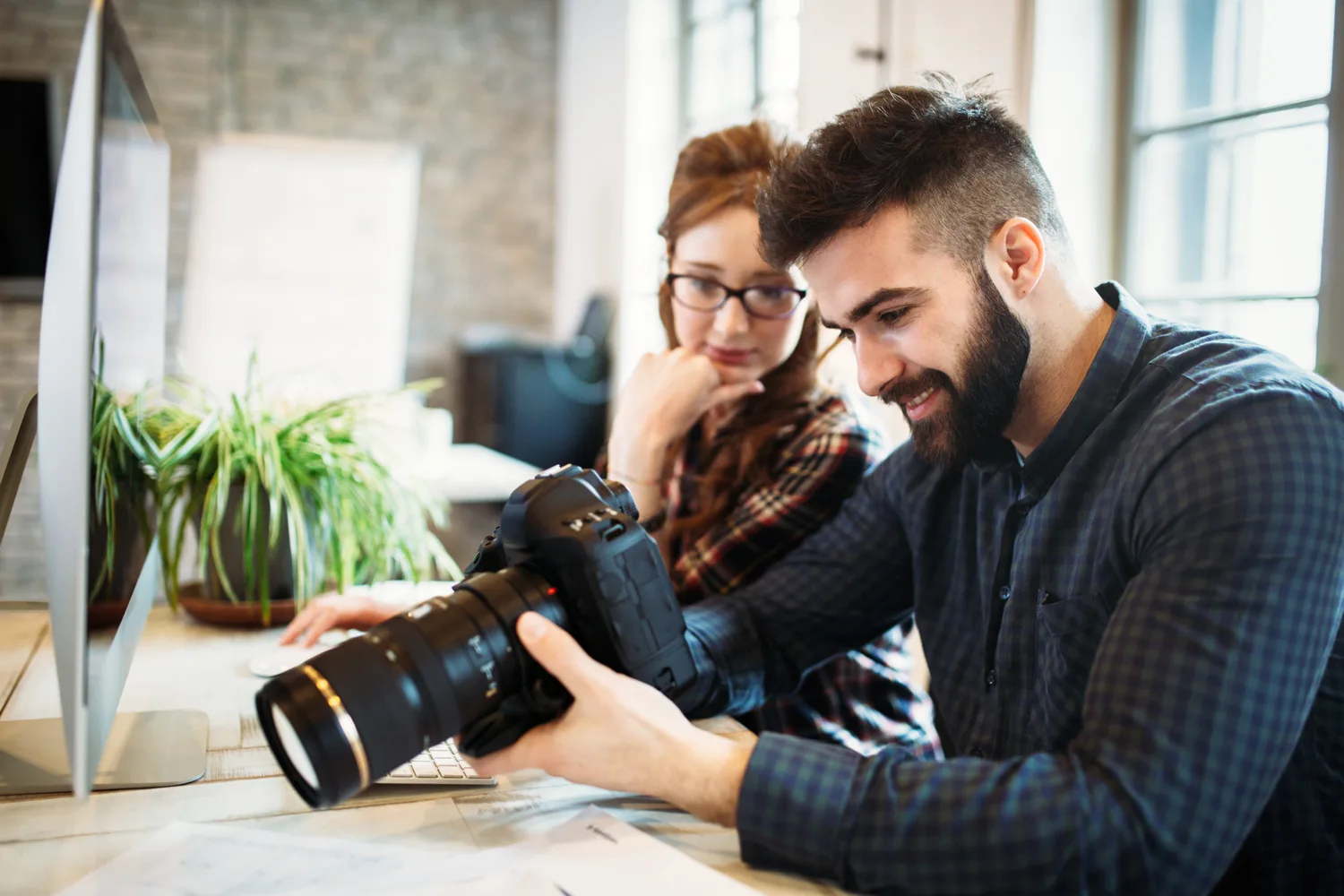 Two people reviewing photos on a DSLR camera in a bright, modern office setting, representing one-on-one photography classes