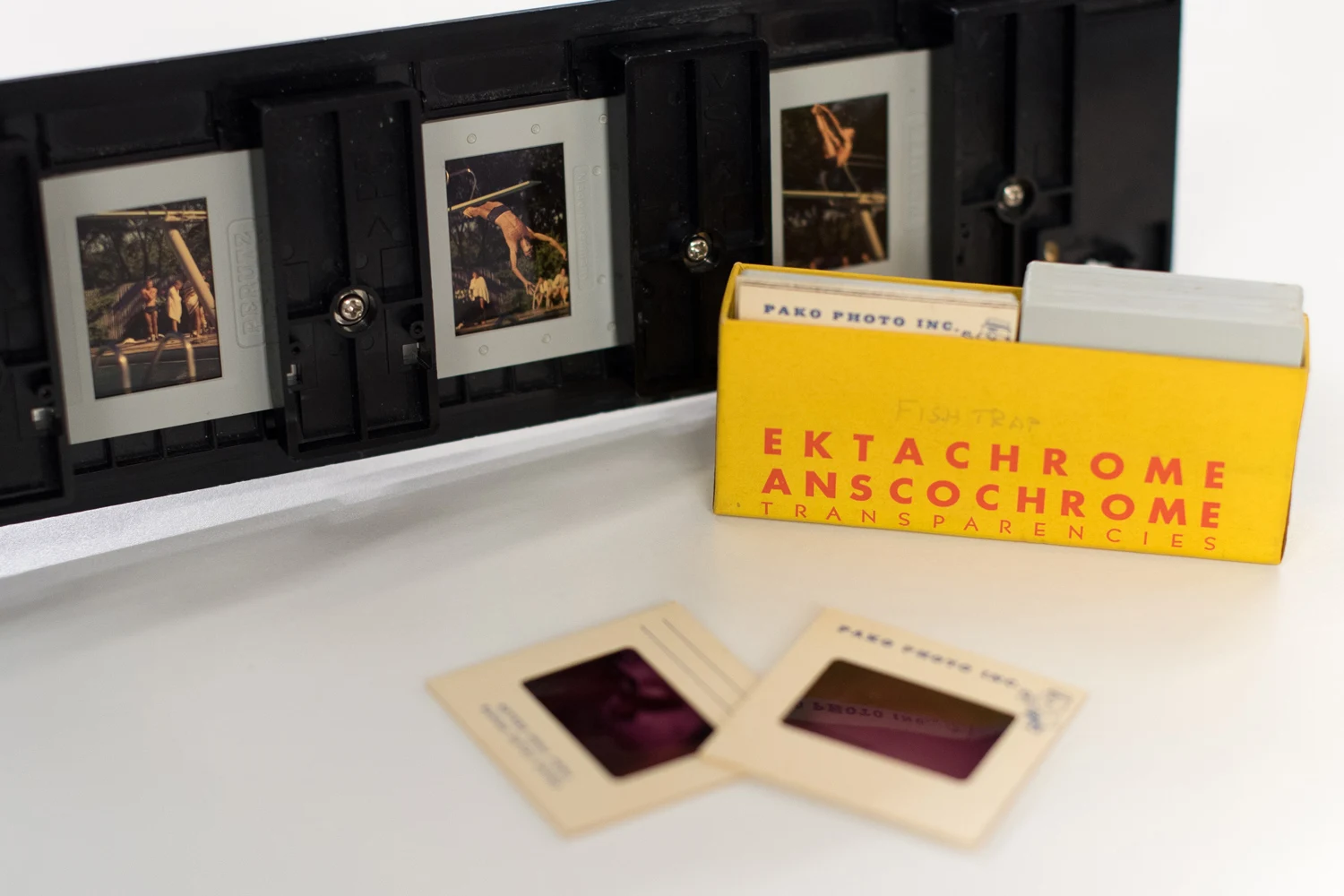 Vintage slide transparencies in a yellow Ektachrome box, with a slide viewer and individual slides displayed on a white surface