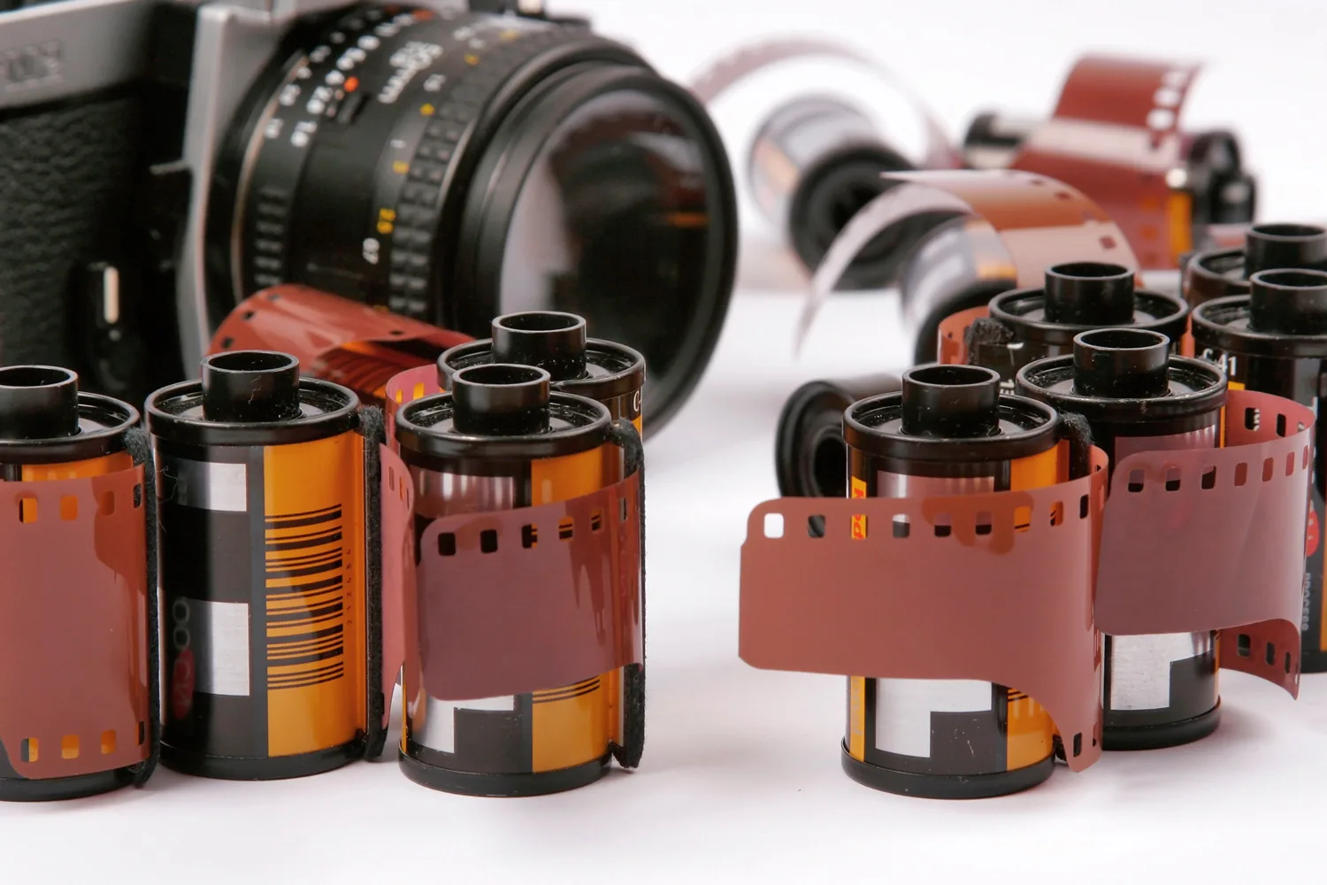 Several rolls of photographic 35mm film, some partially unspooled, with a vintage camera in the background