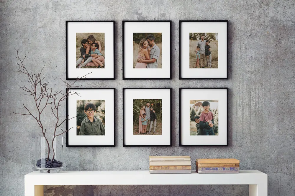 A gallery wall featuring six framed premium art photo prints of family moments, arranged in a grid above a modern white console table