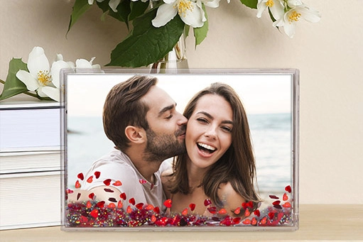 A custom snow globe photo frame featuring a couple smiling by the ocean, with floating red heart-shaped confetti inside the frame