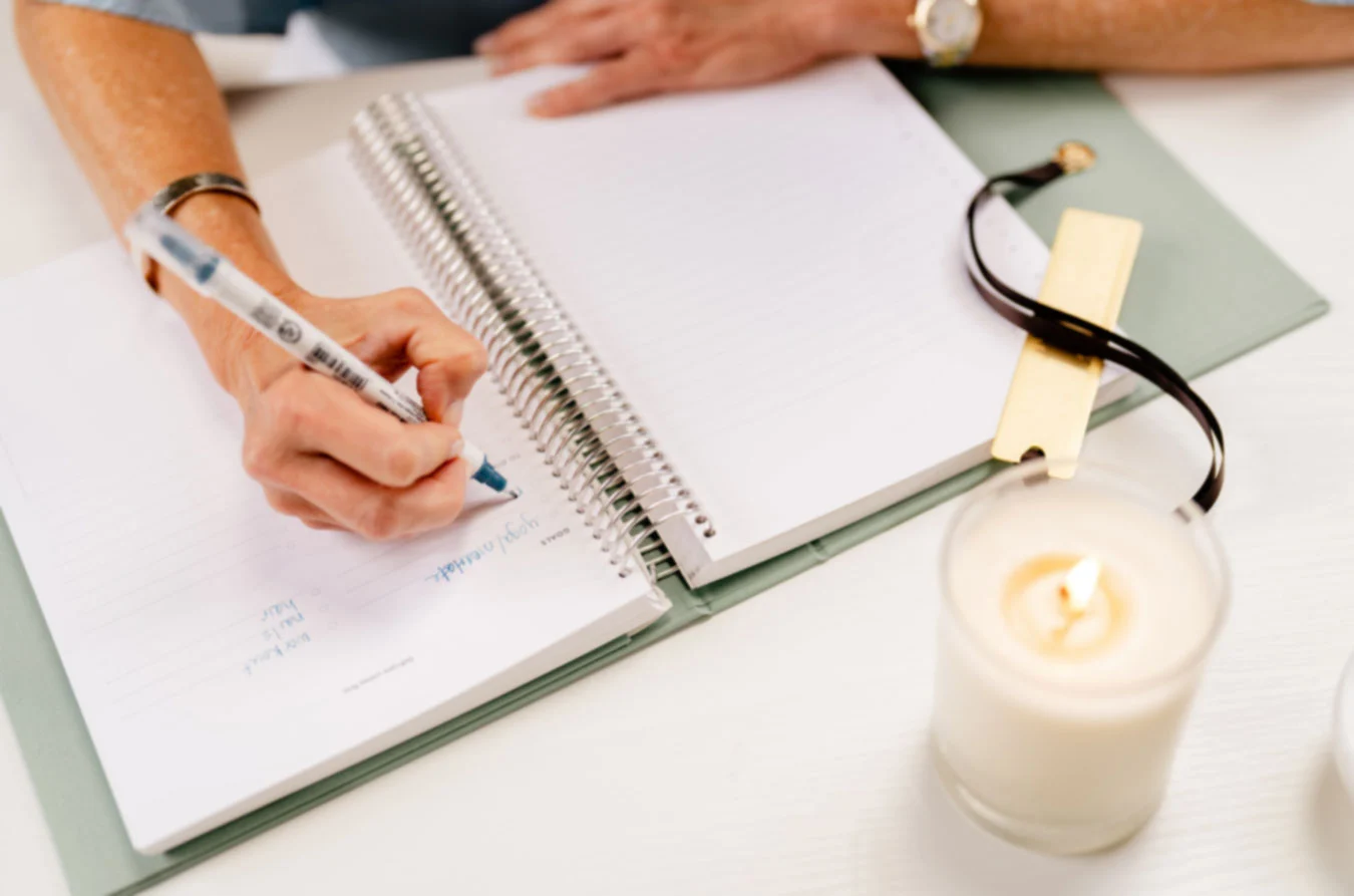 Women writing in Dutch and Deckle Tuscany colored linen planner with Plumeria Soy Lotion Candle lit
