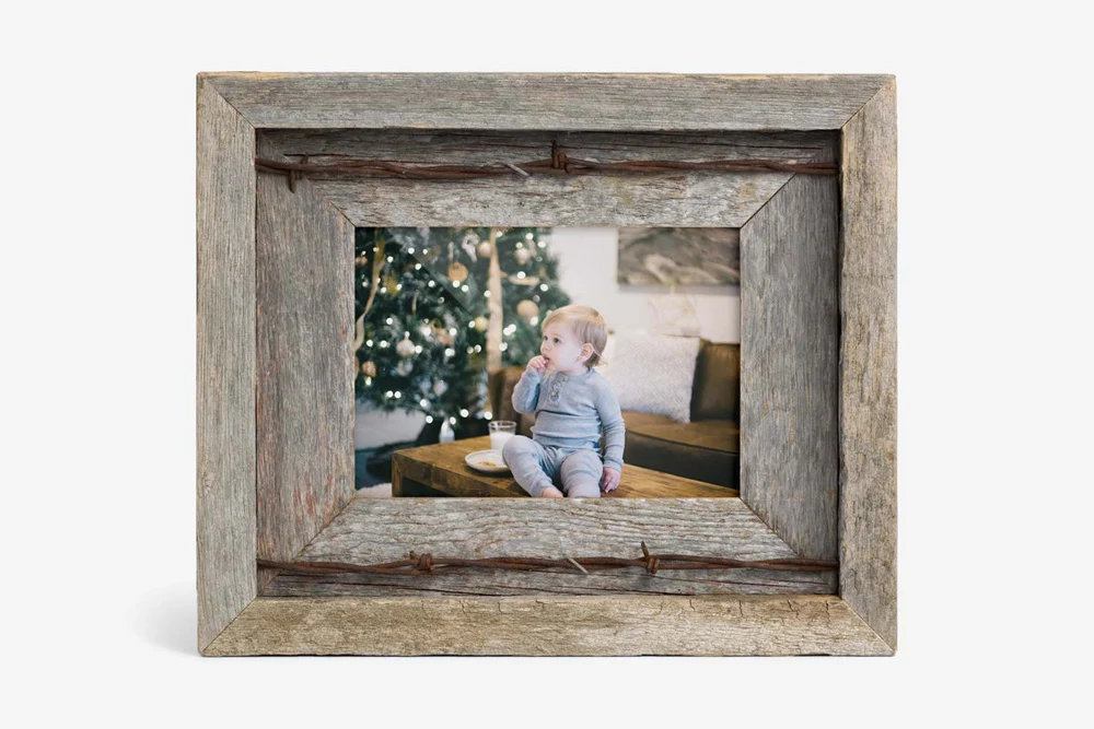 A rustic barn wood photo frame with barbed wire accents, featuring a picture of a child sitting near a Christmas tree