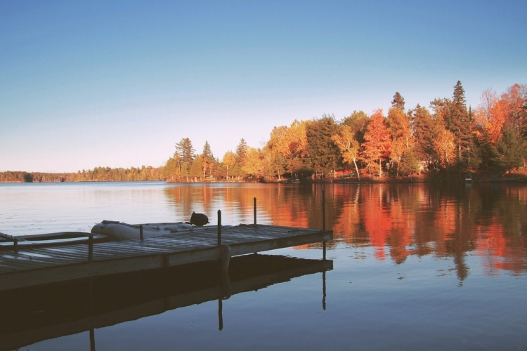 Dock overlooking calm lake with colorful fall foliage reflecting in the water