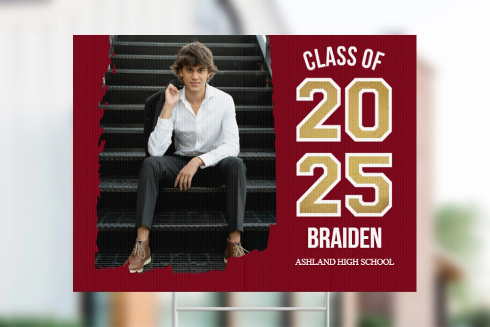 A custom graduation yard sign featuring a senior portrait of a young man sitting on stairs, with Class of 2025 and his name displayed