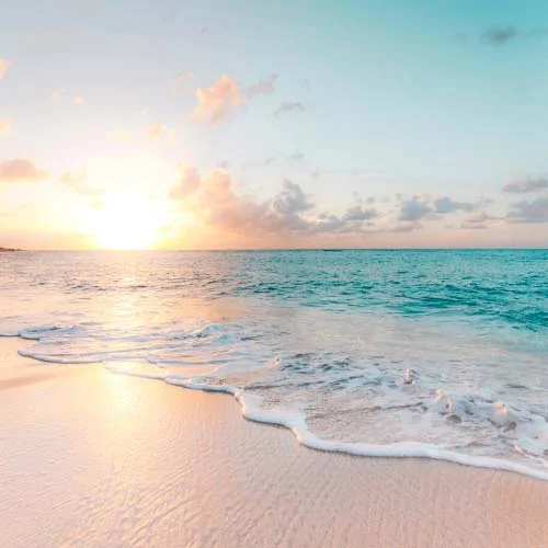 Tropical paradise photo with aqua blue ocean water, sand beach, blue sky, bright sun and clouds