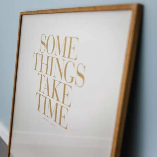 Brown framed picture against blue wall with quote saying some things take time