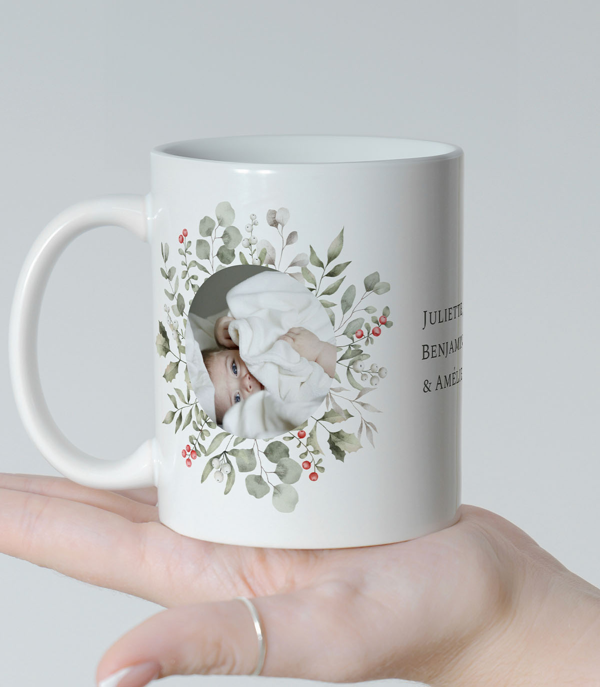 Un mug avec couronne florale composée de houx, de baies rouge et de feuilles d'hiver dans laquelle se trouve une photo.